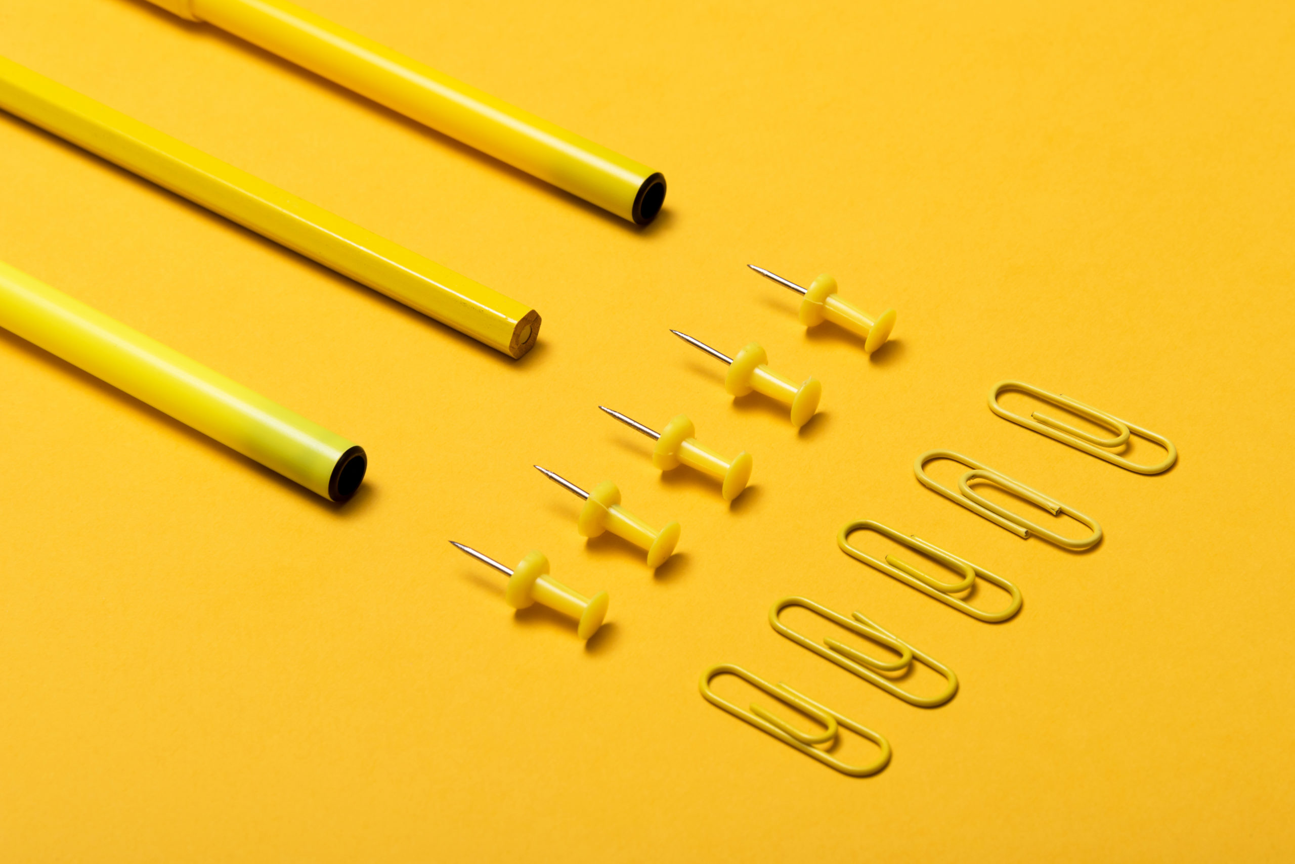 Colourful pencils, thumbtacks and clips over a yellow background